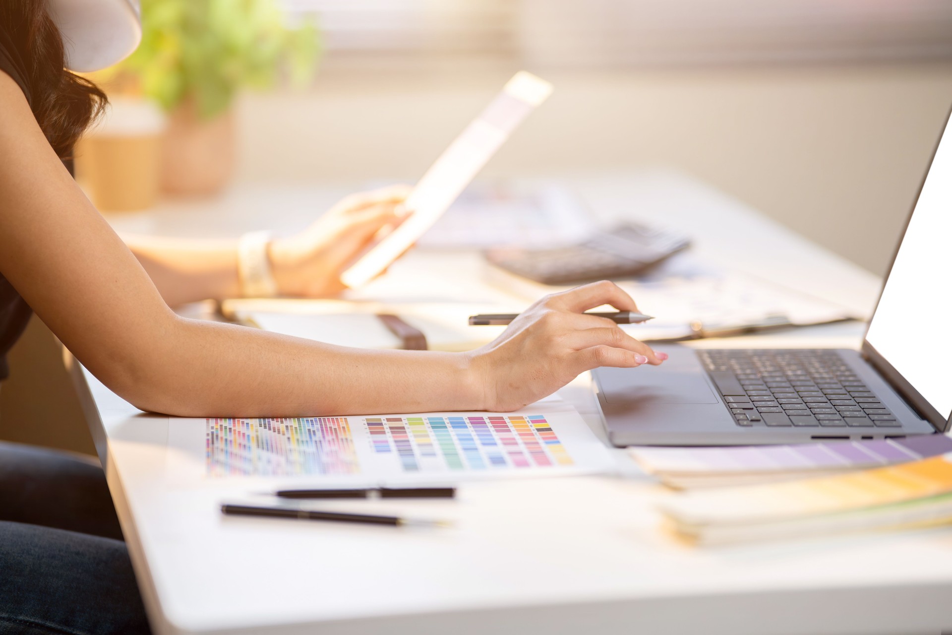 Close up of woman designer holding color chart with pen over laptop sits at office's working table.